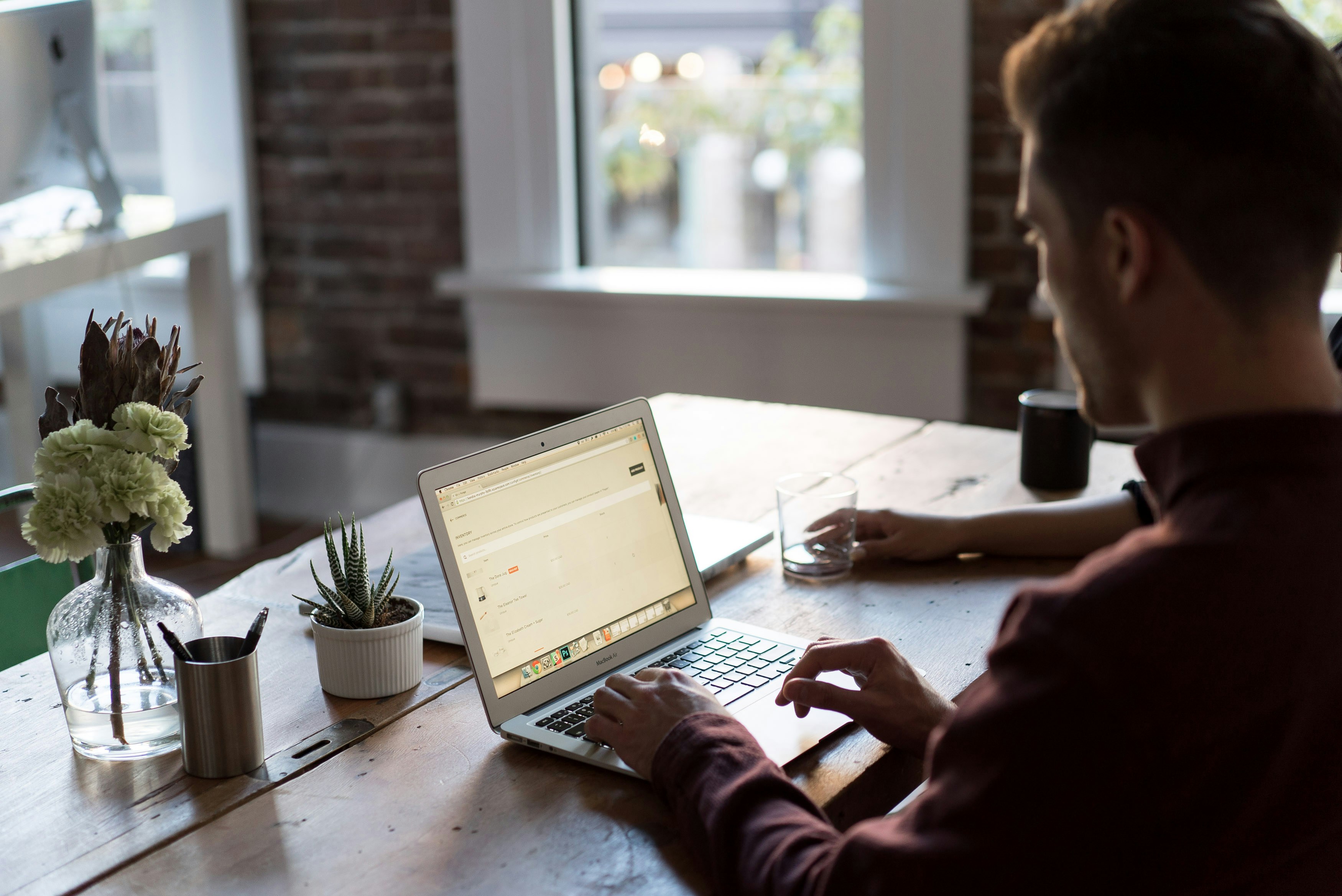 A man works on ecommerce website development at a wooden desk in a modern, sunlit office with brick walls and large windows. His laptop screen displays a scheduling tool or calendar. The desk features a vase with flowers, a small succulent, pens in a metal cup, and a glass of water. Another person's arm is partially visible across the table. Let me know if you'd like a shorter version or a variation focused more on the digital/UX aspect. A man works on ecommerce website development at a wooden desk in a modern, sunlit office with brick walls and large windows. His laptop screen displays a scheduling tool or calendar. The desk features a vase with flowers, a small succulent, pens in a metal cup, and a glass of water. Another person's arm is partially visible across the table. Let me know if you'd like a shorter version or a variation focused more on the digital/UX aspect. A man works on ecommerce website development at a wooden desk in a modern, sunlit office with brick walls and large windows. His laptop screen displays a scheduling tool or calendar. The desk features a vase with flowers, a small succulent, pens in a metal cup, and a glass of water. Another person's arm is partially visible across the table.